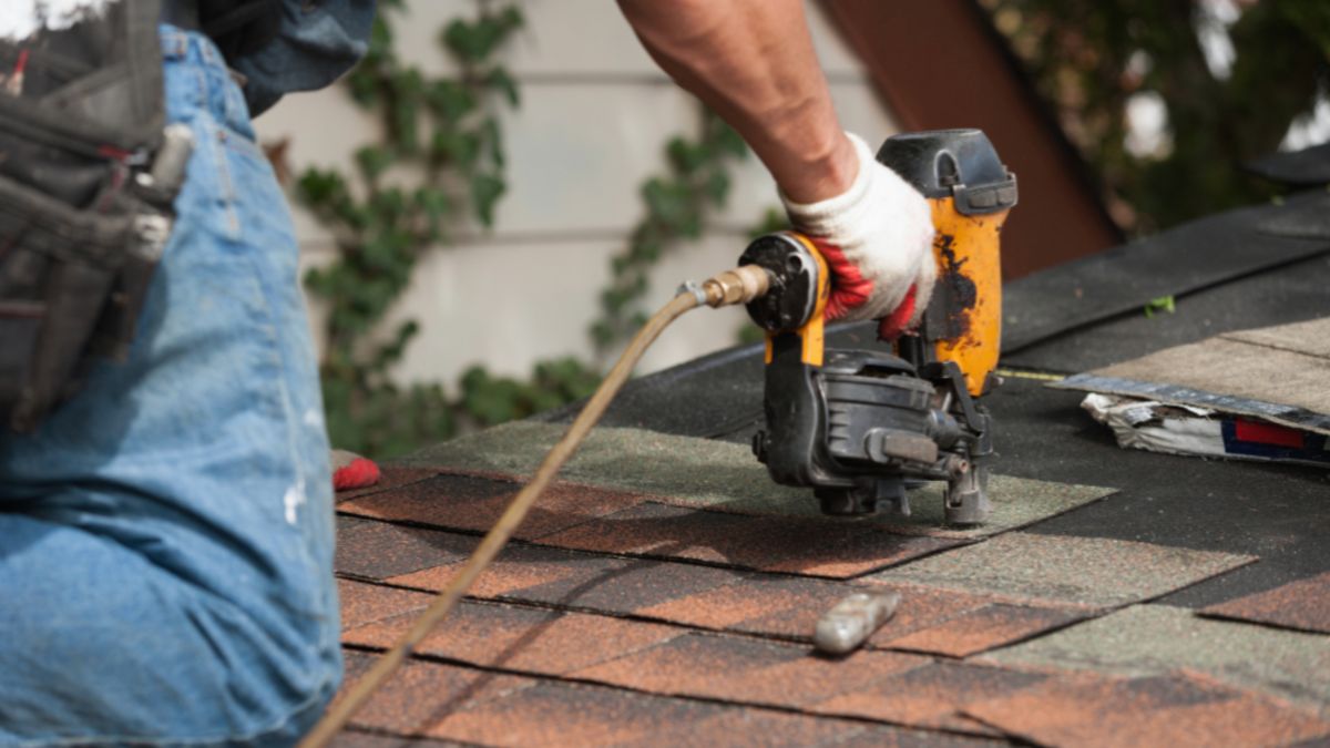 A man performs emergency roof repair using a nailer to secure roofing materials in place.