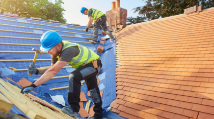 Two roofing contractors in Beaufort, SC, using hammers to repair a residential roof under sunny conditions.