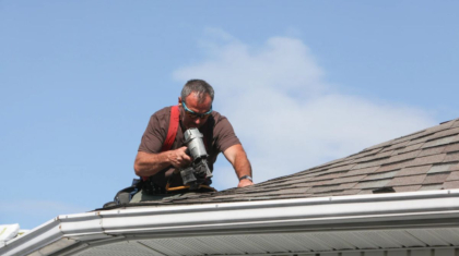 A roofing contractor using a nail gun on a shingle roof, representing the work involved when warning signs suggest replacement is needed.