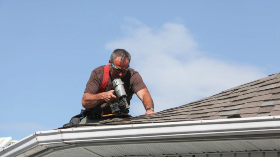 A roofing contractor using a nail gun on a shingle roof, representing the work involved when warning signs suggest replacement is needed.