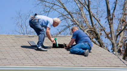 Roofers applying sealant around a vent on a shingle roof.