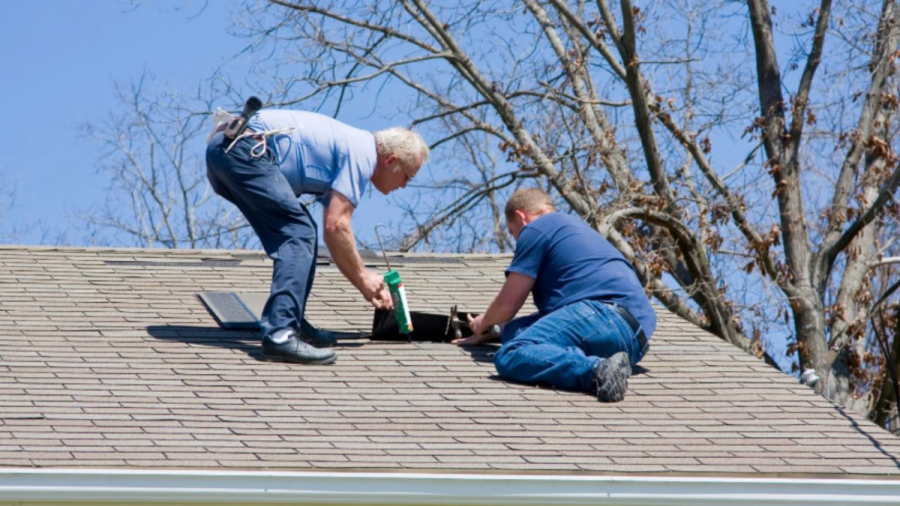 Roofers applying sealant around a vent on a shingle roof.