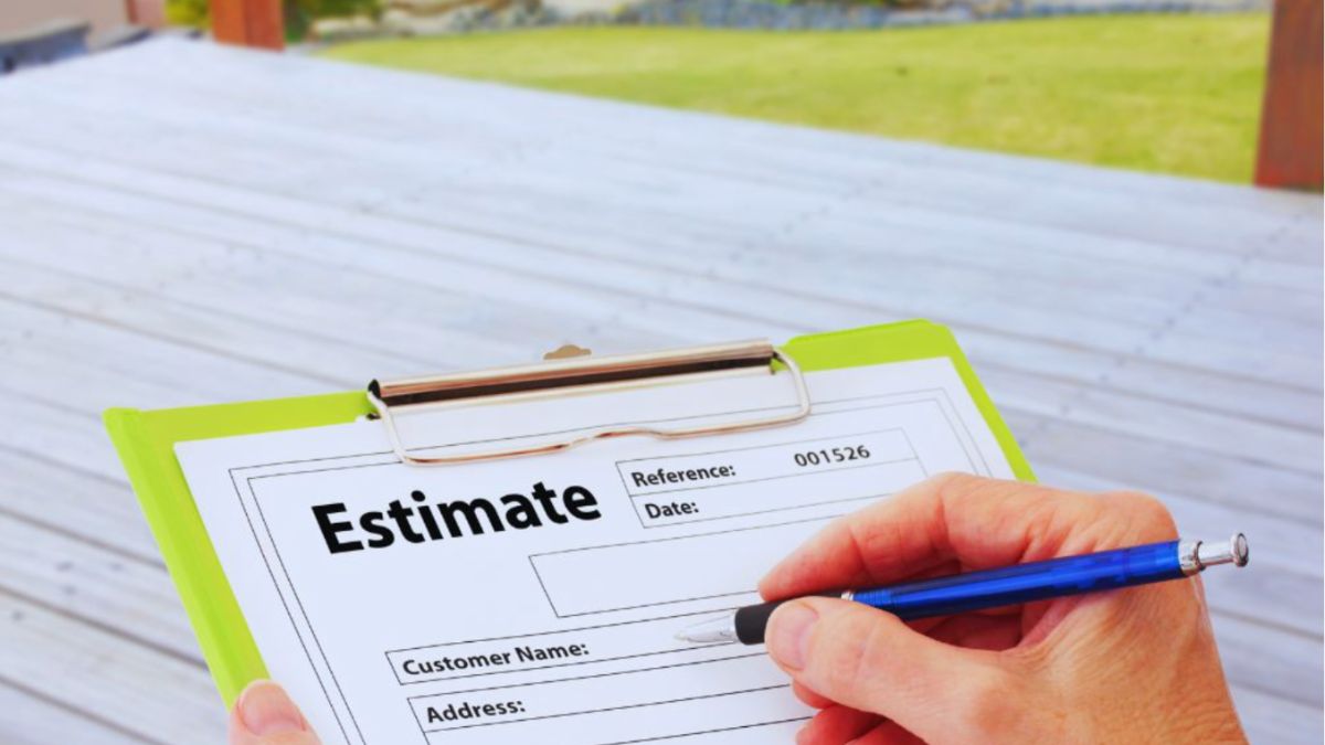 Close-up of a person filling out a roofing estimate form on a clipboard, with a wooden deck and lawn in the background.