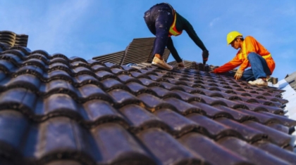 Two men engaged in roof repair work with a vibrant blue sky in the background, highlighting local repair services.