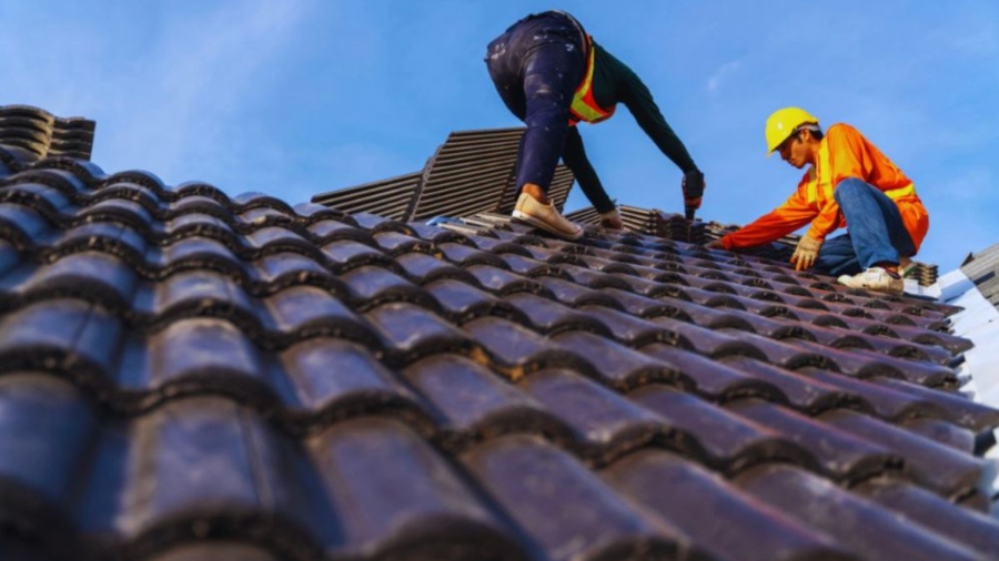 Two men engaged in roof repair work with a vibrant blue sky in the background, highlighting local repair services.