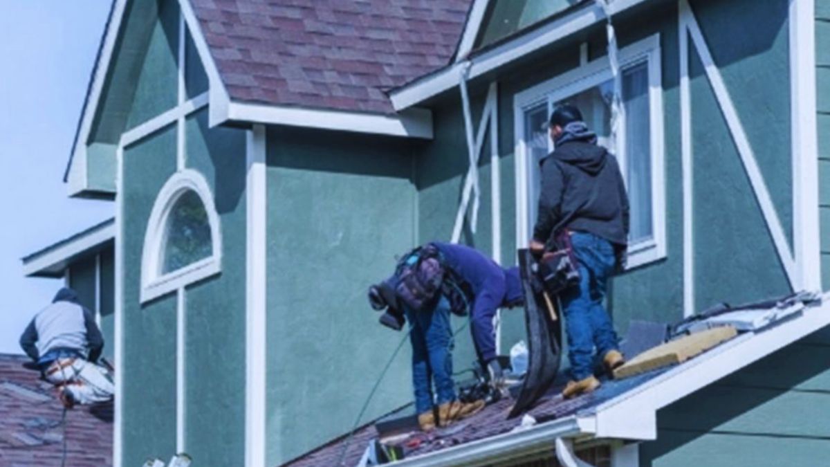 Roofers are actively working on top of a green house in Jasper County, SC, using safety equipment and various tools to repair and maintain shingles, illustrating professional roof repair services in progress.