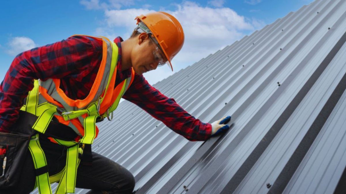 A roofing contractor wearing safety gear inspects a metal roof under a clear blue sky, representing residential roofing services in Hardeeville, SC.
