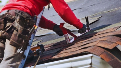 A man repairs a roof using a tool, demonstrating skilled roofing work in progress.