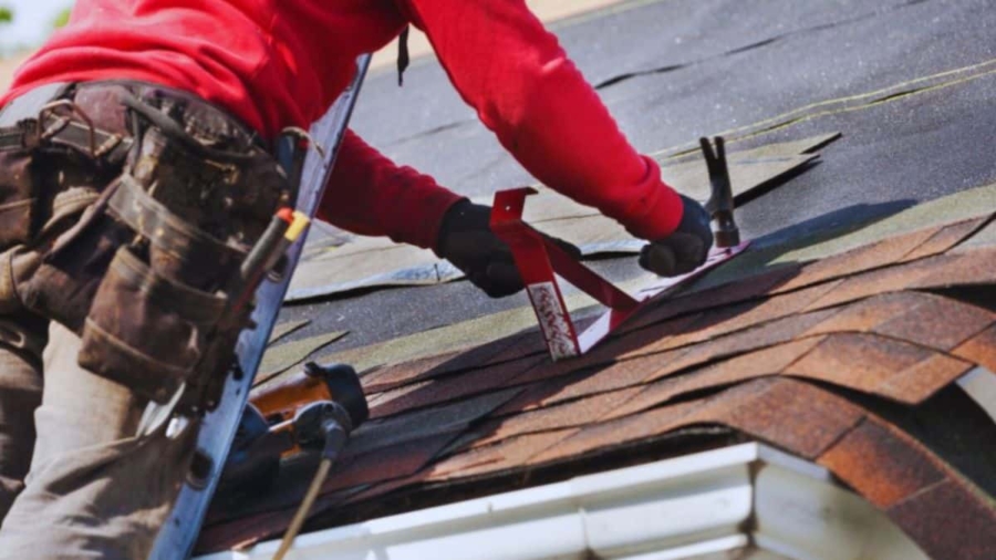 A man repairs a roof using a tool, demonstrating skilled roofing work in progress.