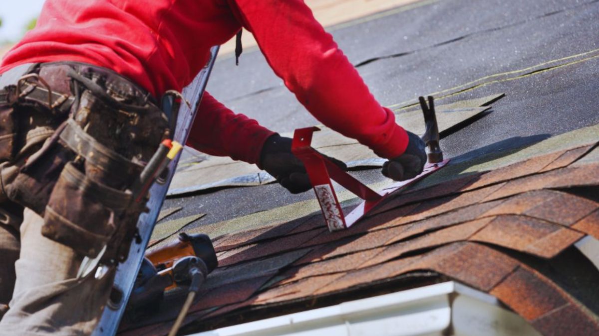 Roofer securing damaged asphalt shingles with a cordless driver during an emergency roof repair.