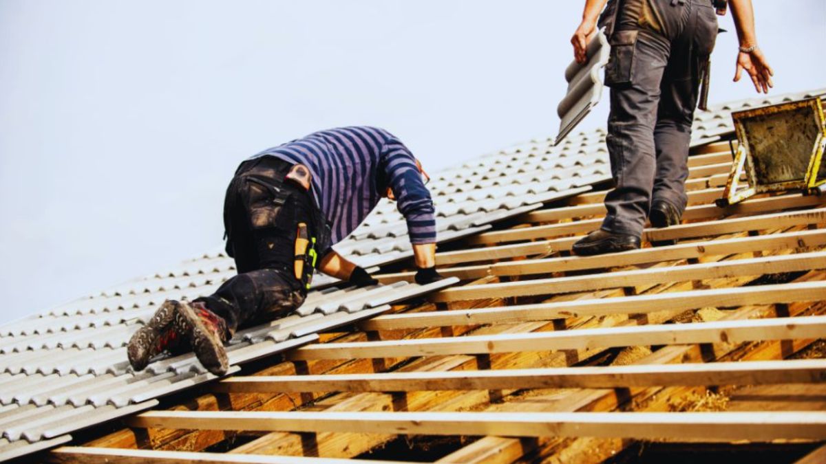 Roof installation showing professional contractors installing roofing tiles on a residential structure, working on wooden roof framing with proper tools and equipment.