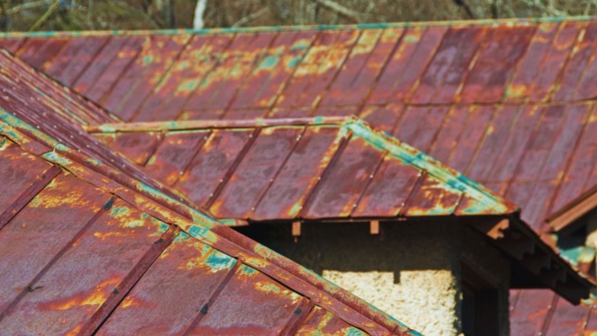 Close-up view of an old metal roof with heavy rust, discoloration, and corrosion on multiple roof slopes, illustrating the need for professional rusty roof repair and replacement.