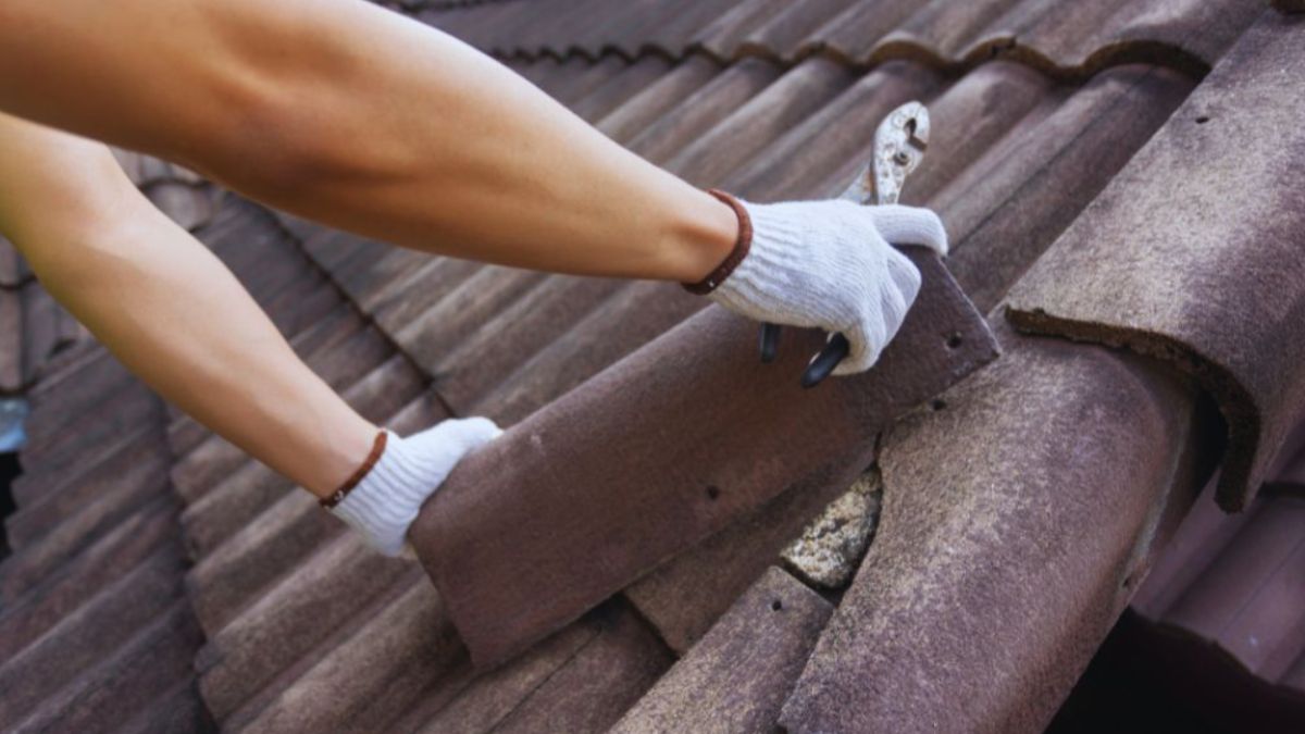 Close-up of a worker’s gloved hands lifting and replacing damaged brown clay roof tiles during a tile roof repair.