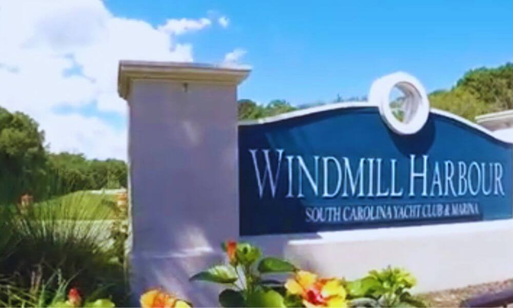 Entrance sign for Windmill Harbour, Hilton Head Island, South Carolina, yacht club and marina surrounded by landscaping and greenery under a bright blue sky.