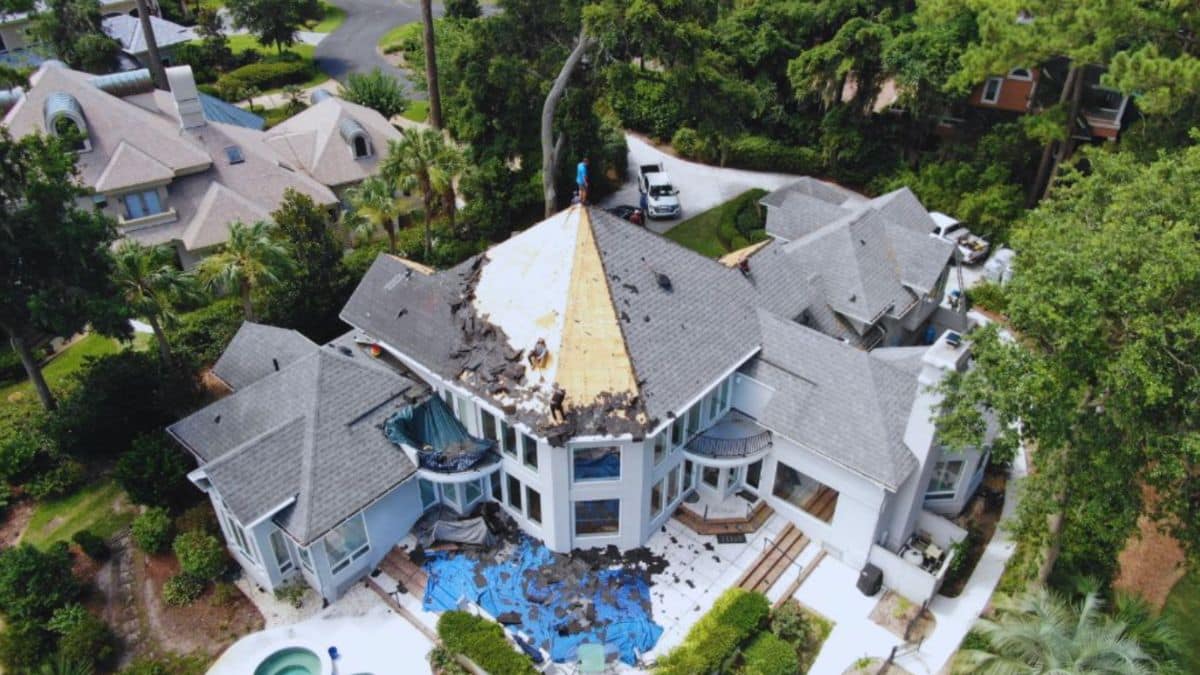 Aerial view of major roof repair on a large coastal home in Hilton Head Island, SC, with workers removing damaged shingles and decking after storm damage.