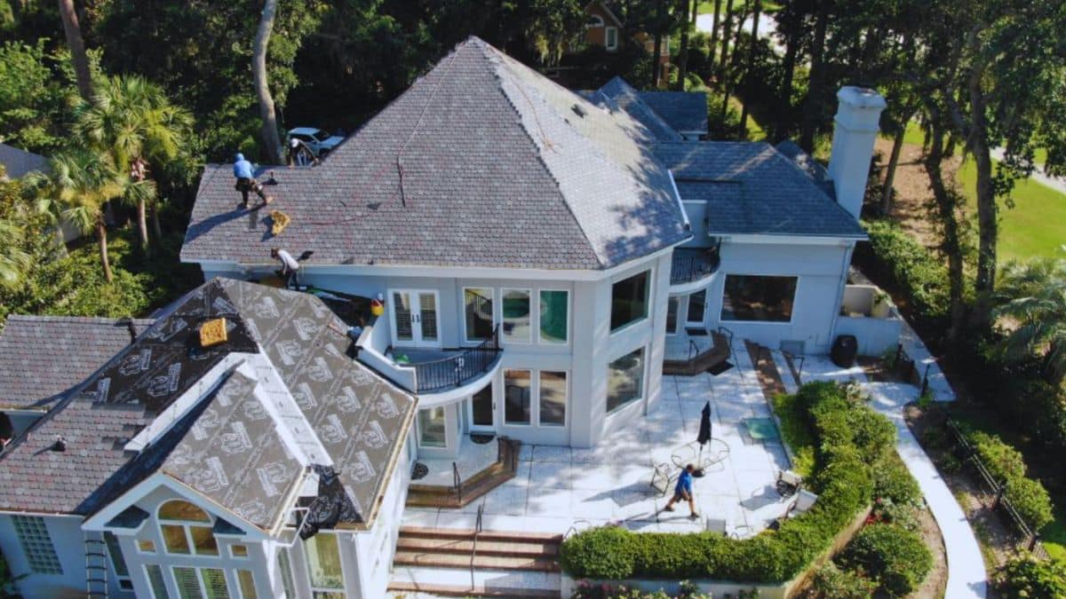 Roofing contractors in Bluffton replacing and repairing a large residential roof on a luxury home with workers installing shingles and underlayment.