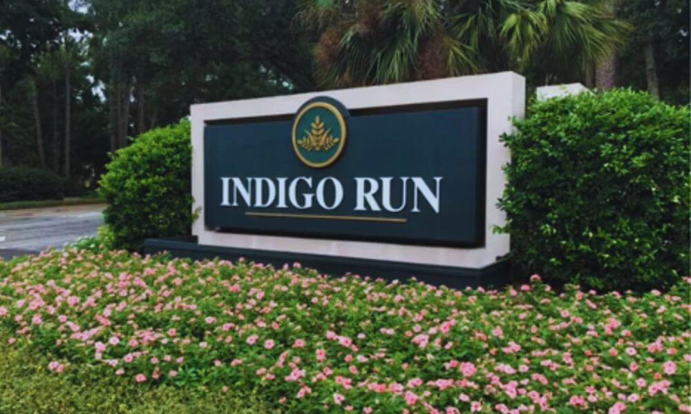 Entrance sign for Indigo Run Plantation in Hilton Head Island, SC, surrounded by lush landscaping, palm trees, and blooming flowers.