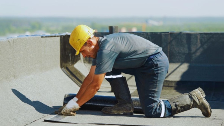 Roofing contractor installing a waterproof membrane on a flat roof.