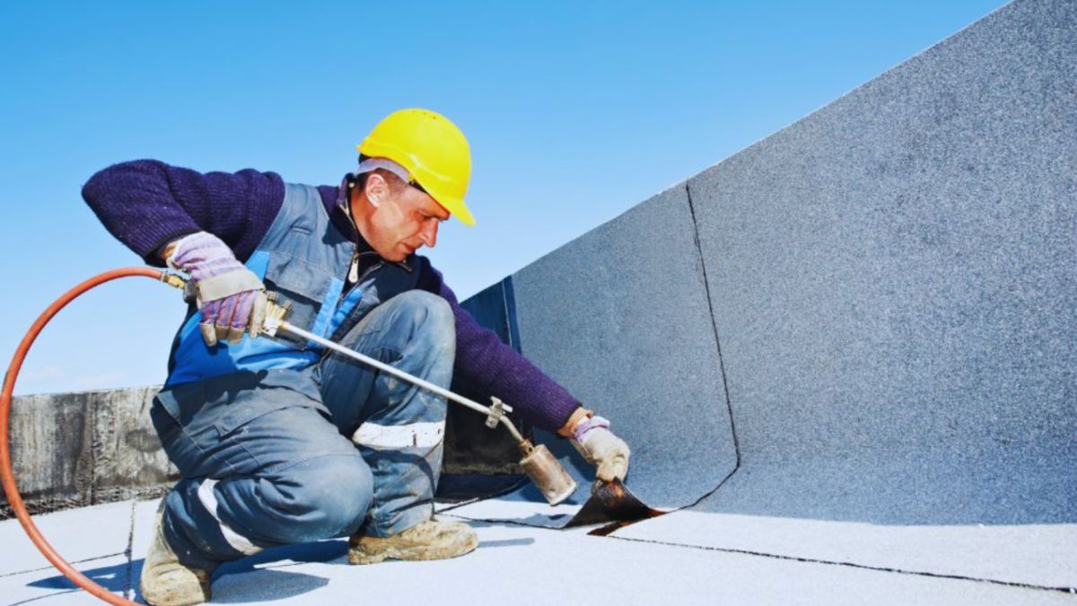 Contractor using a torch to repair a damaged flat roof membrane, addressing common flat roof problems such as seam separation and leaks.