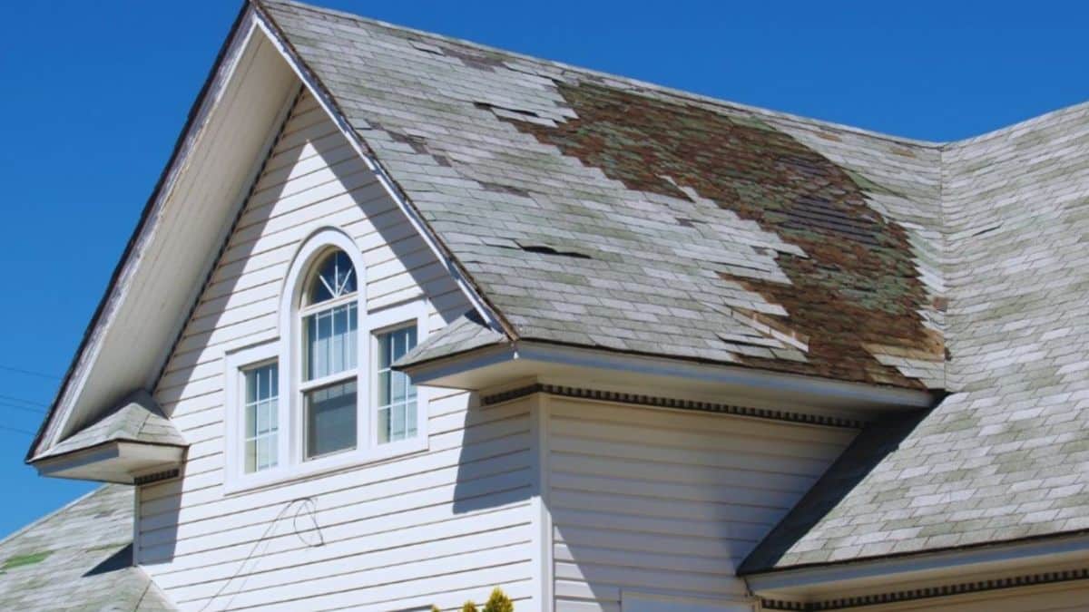 Damaged slate roof with missing, cracked, and deteriorating tiles on a residential home.